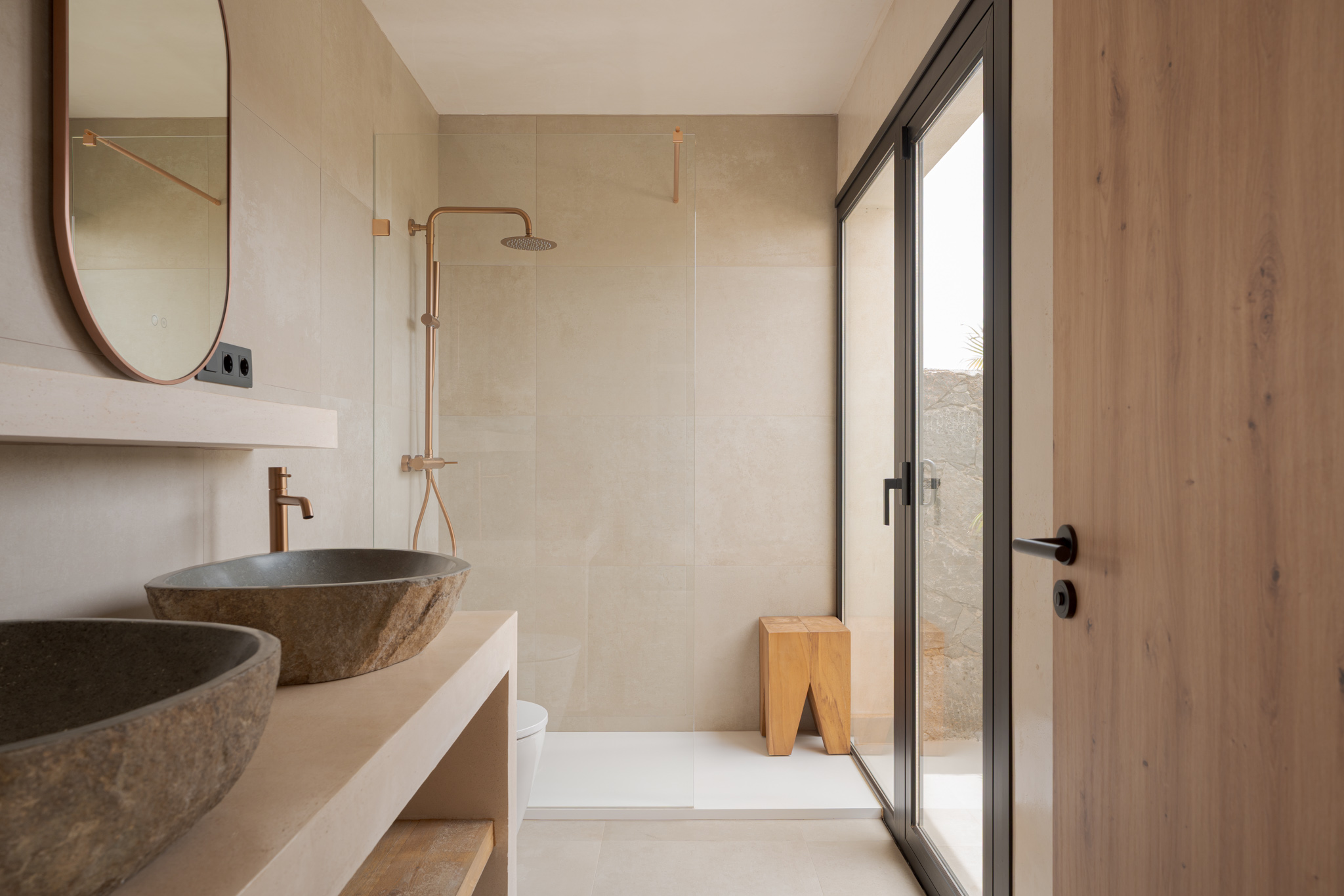 Bathroom with stone basin, copper rain shower and glass door to private patio